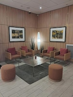 Uma área de estar moderna com uma mesa de centro, quatro poltronas e dois pufes redondos.