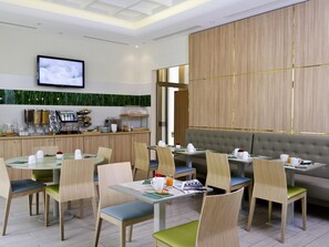 Un comedor moderno con mesas, sillas, una estación de buffet y una pantalla de televisión.