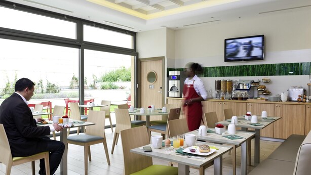A hotel dining area with tables, chairs, a coffee machine, and a TV mounted on the wall.