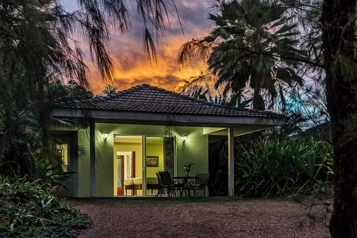 Une petite maison moderne avec un toit en tuiles, une porte d’entrée en verre et un patio aménagé avec des chaises et une table.