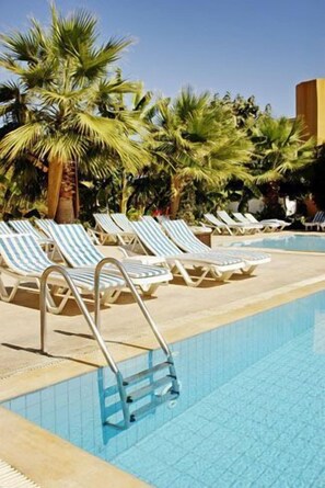 Un espace aménagé au bord de la piscine, avec des chaises longues et des palmiers.