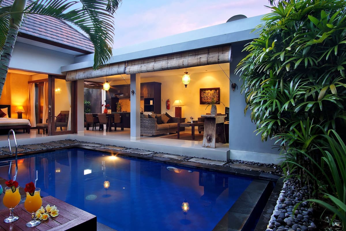 Un área de piscina moderna con piscina cristalina, mobiliario de salón y zona de comedor.
