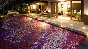 A hotel with a swimming pool surrounded by flower petals, a covered outdoor seating area, and a well-lit interior.