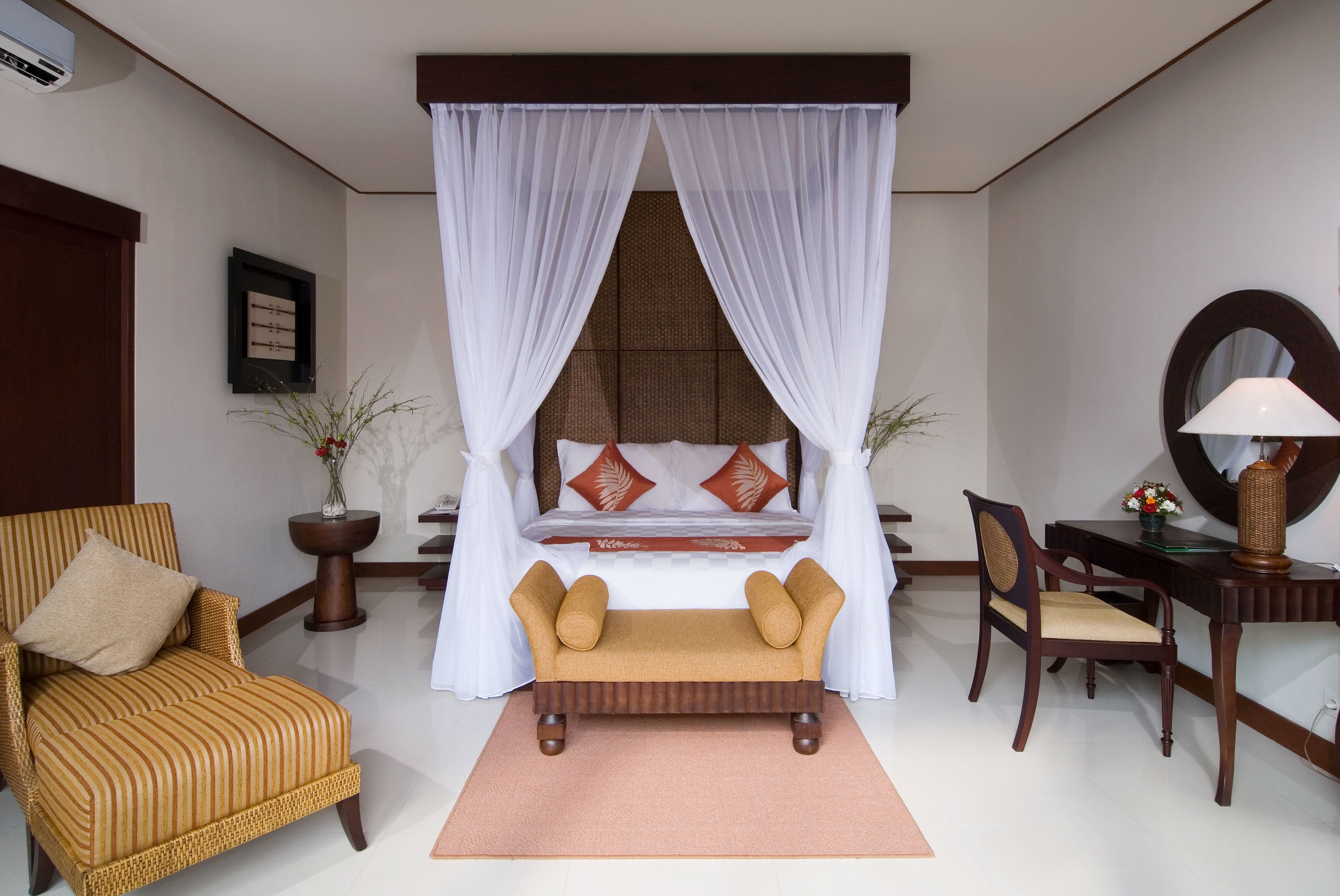 A bedroom with a canopy bed, a sofa, a chair, a desk, and a mirror.