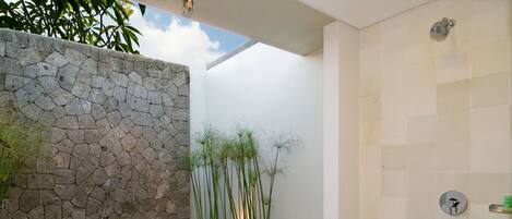 A modern bathroom with a stone wall, a bathtub with colorful pebbles, and a shower area.