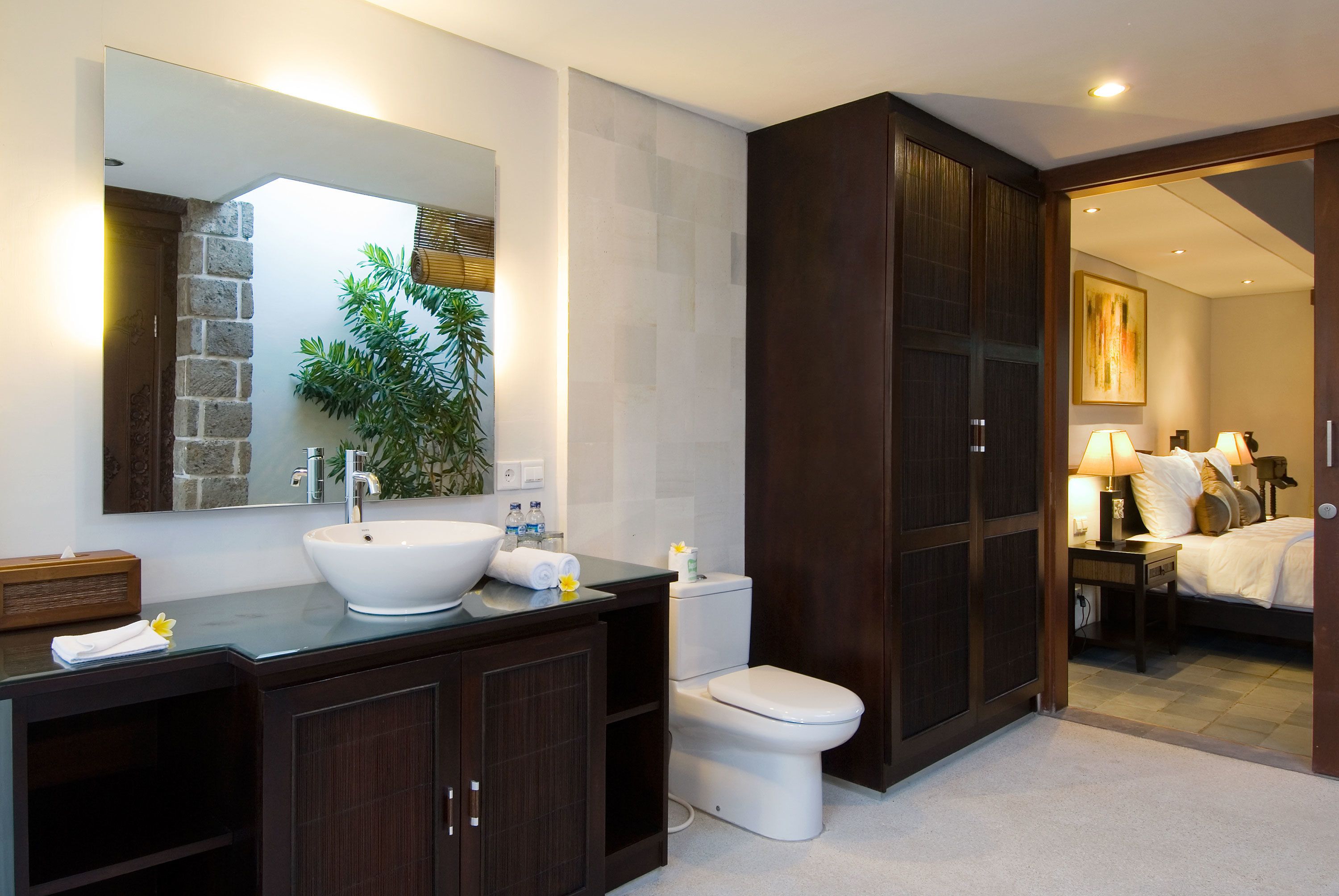 Un baño moderno con un espejo grande, un lavabo blanco, armarios de madera oscura y un inodoro.