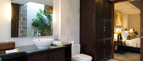 Un baño moderno con un espejo grande, un lavabo blanco, armarios de madera oscura y un inodoro.