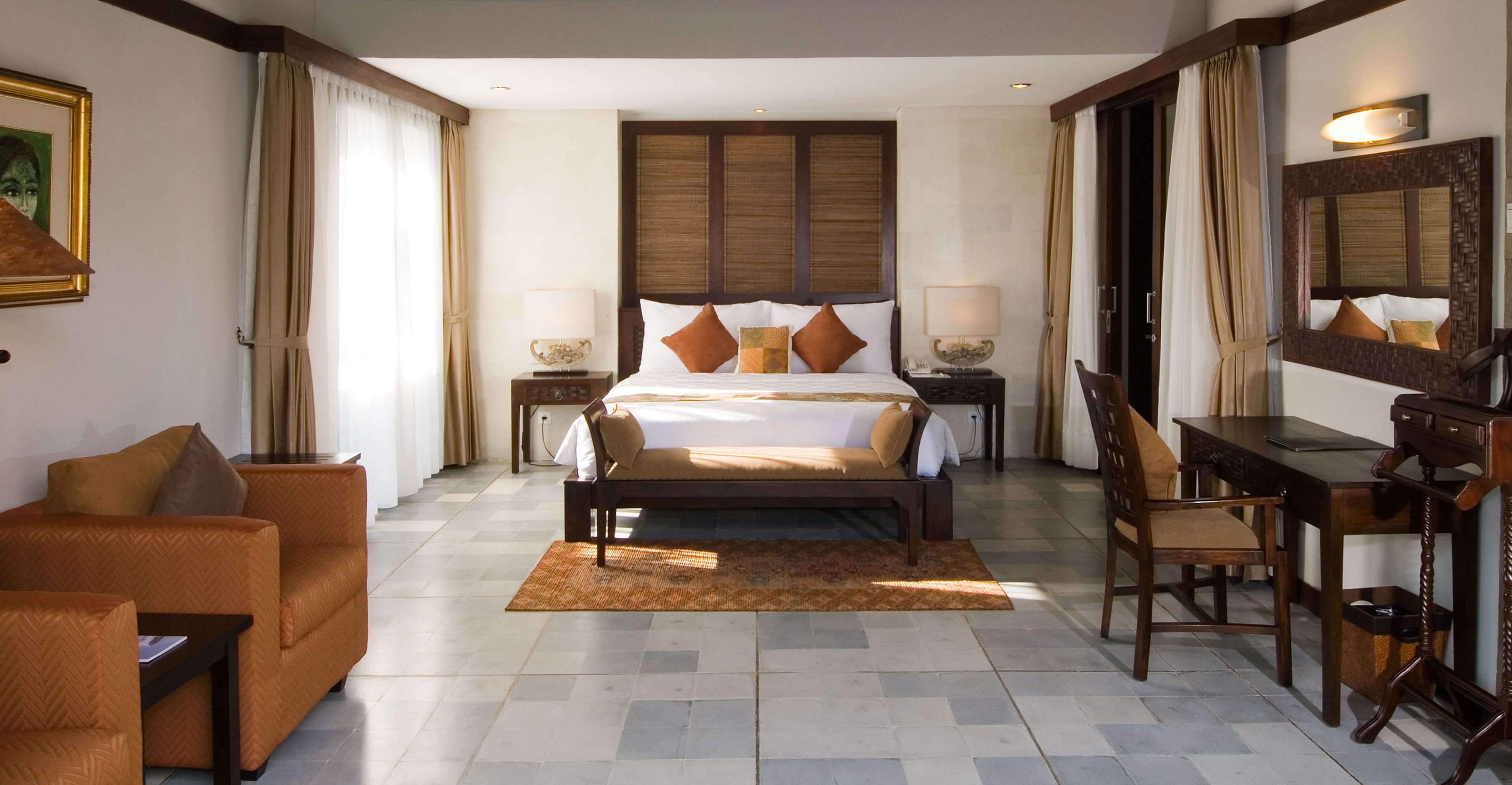 A hotel room with a bed, a desk, a chair, a sofa, and a large mirror.