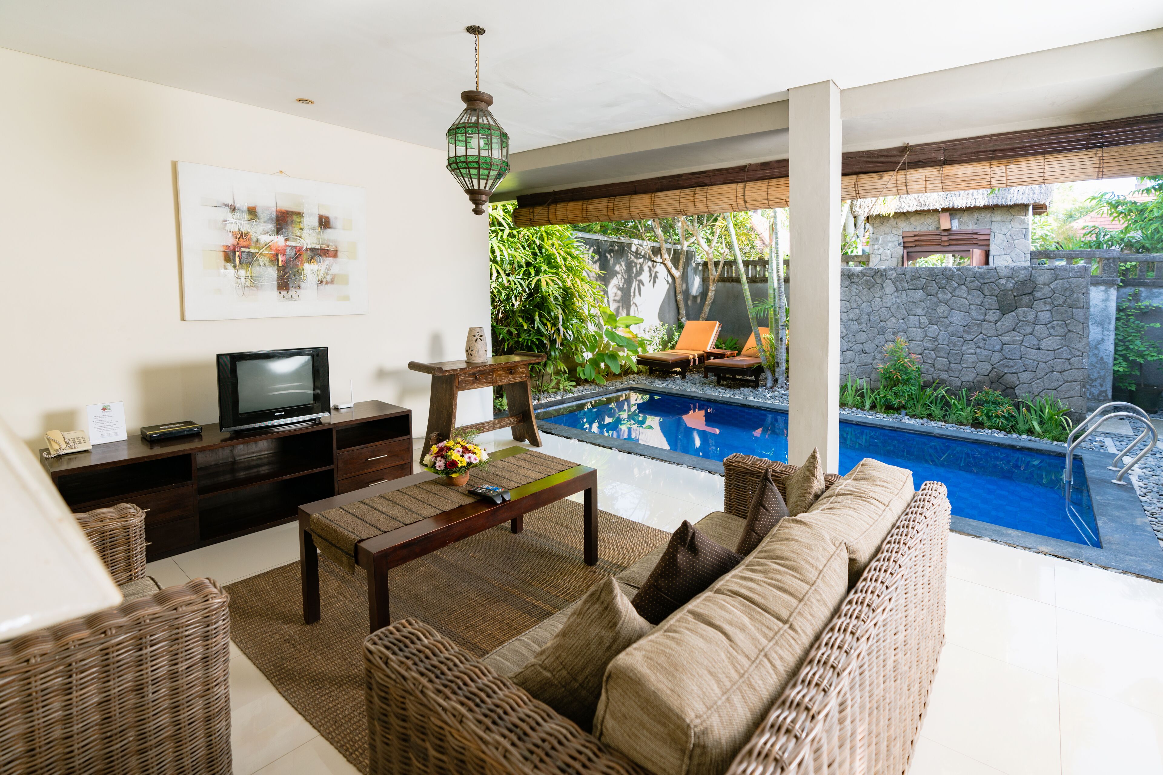 Una sala de estar con televisor, muebles de mimbre y vista a una piscina.