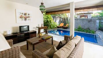 Una sala de estar con televisor, muebles de mimbre y vista a una piscina.