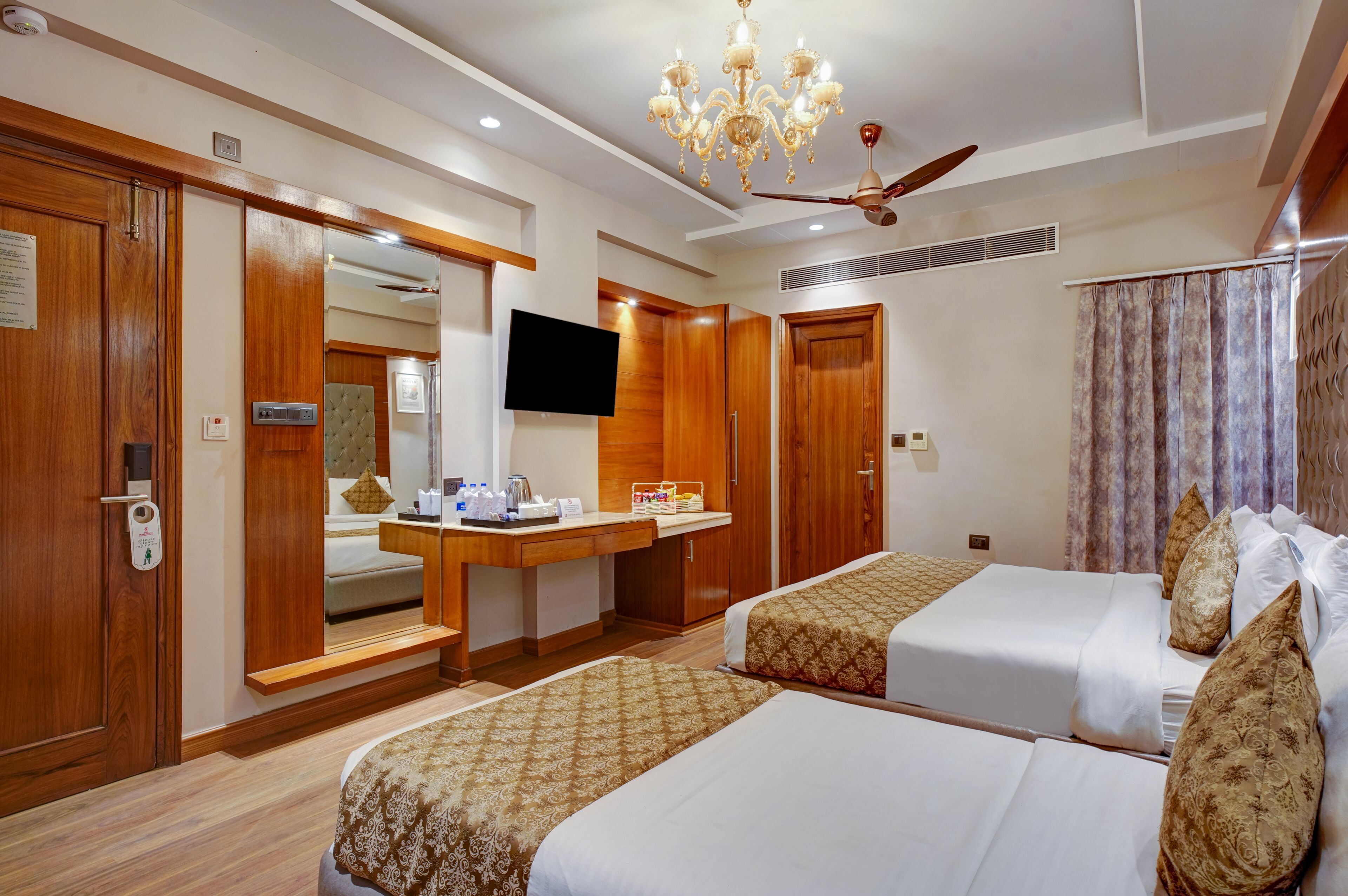 Quarto de hotel com duas camas, televisão, escrivaninha e espelho.