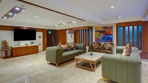 Una sala de estar moderna con televisor de pantalla plana, sofás verdes, una mesa de centro y un cuadro grande.