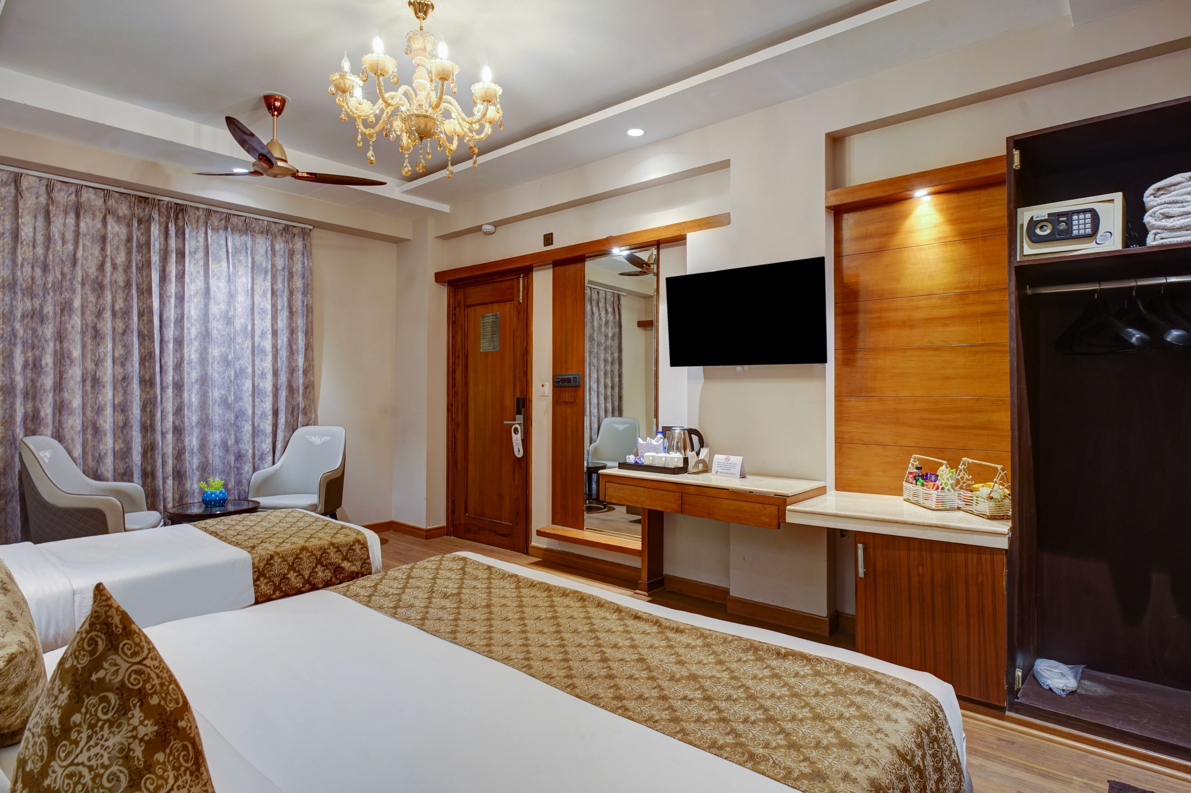 A hotel room with two beds, a desk, a TV, a wardrobe, and a chandelier.