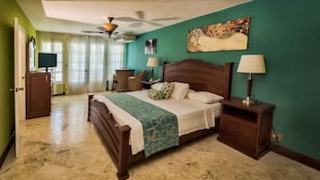 A bedroom with a bed, nightstands, a desk, a chair, a ceiling fan, and a painting on the wall.