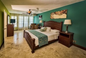 A bedroom with a bed, nightstands, a desk, a chair, a ceiling fan, and a painting on the wall.