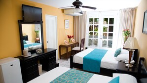 A hotel room with two beds, a desk, a chair, a television, and a ceiling fan.