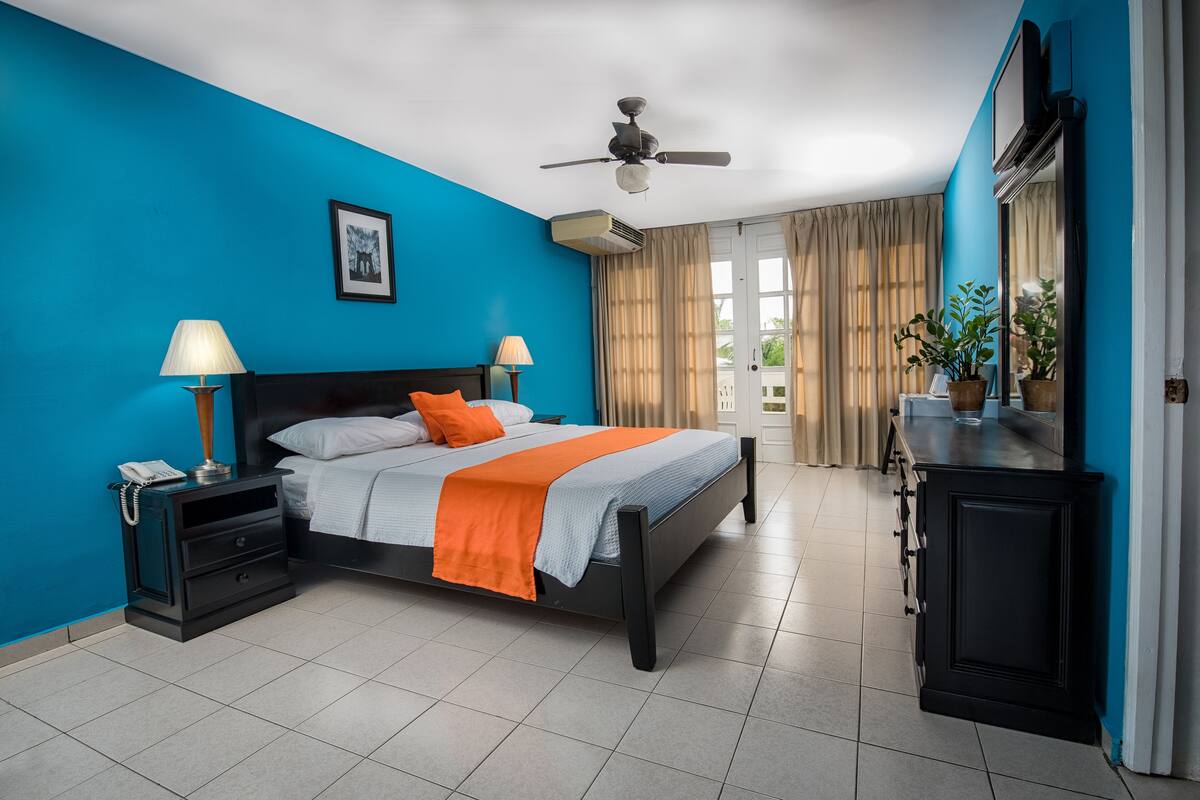 A modern hotel room with a bed, nightstands, a desk, and a ceiling fan.