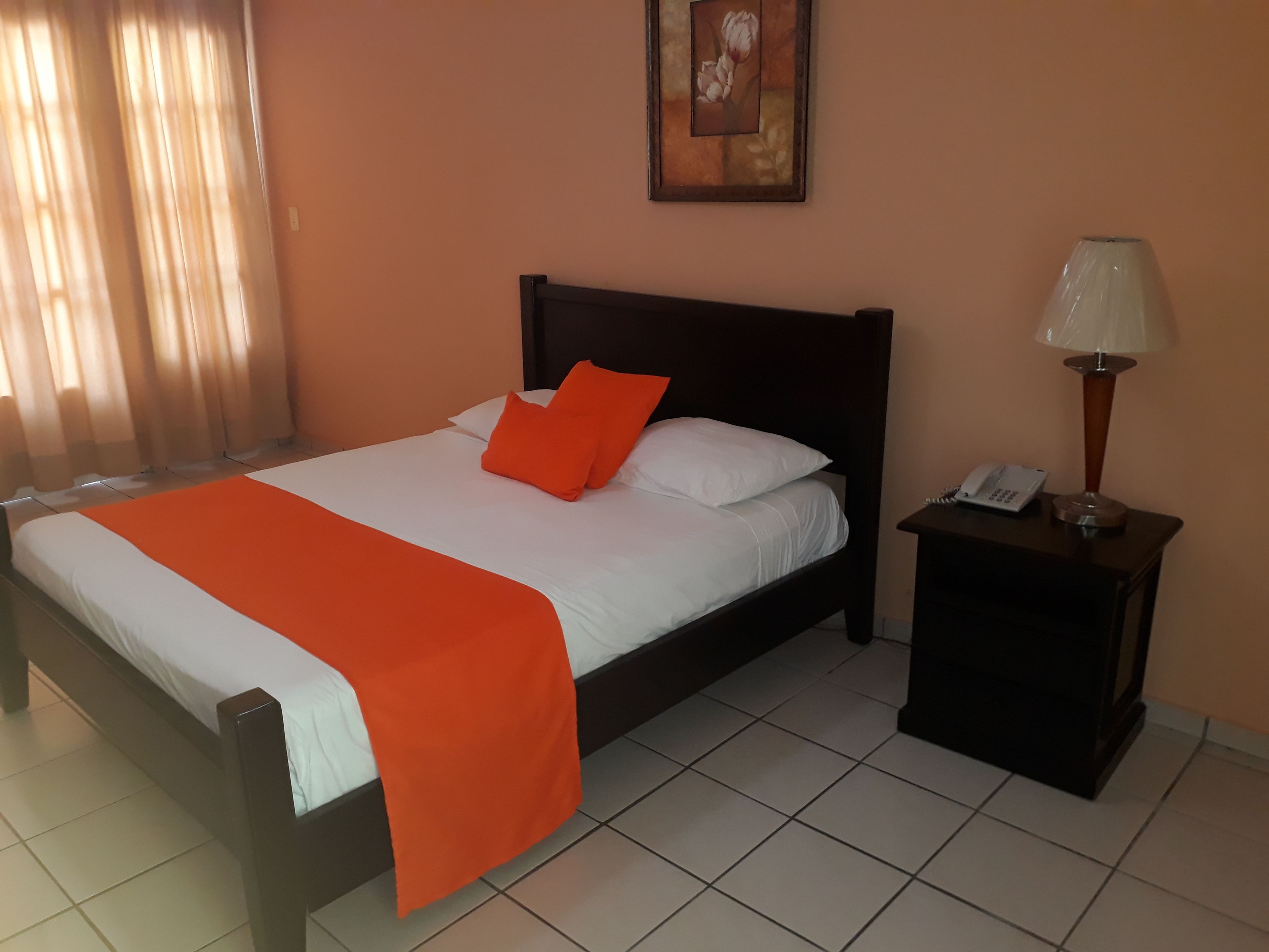 A neatly made bed with an orange blanket, a bedside lamp, and a phone on a nightstand.