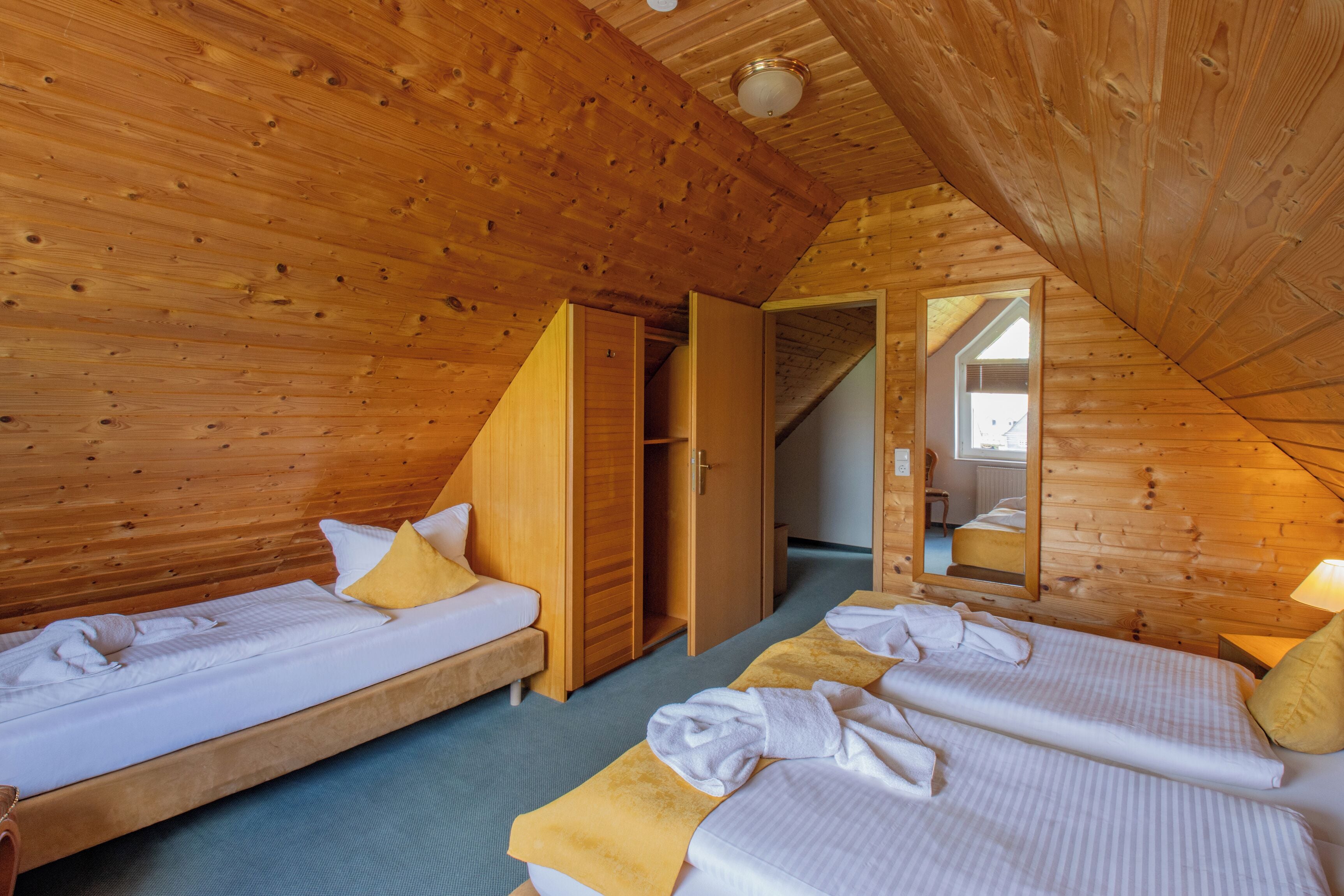 A wooden interior with two beds, a mirror, and a door leading to another room.