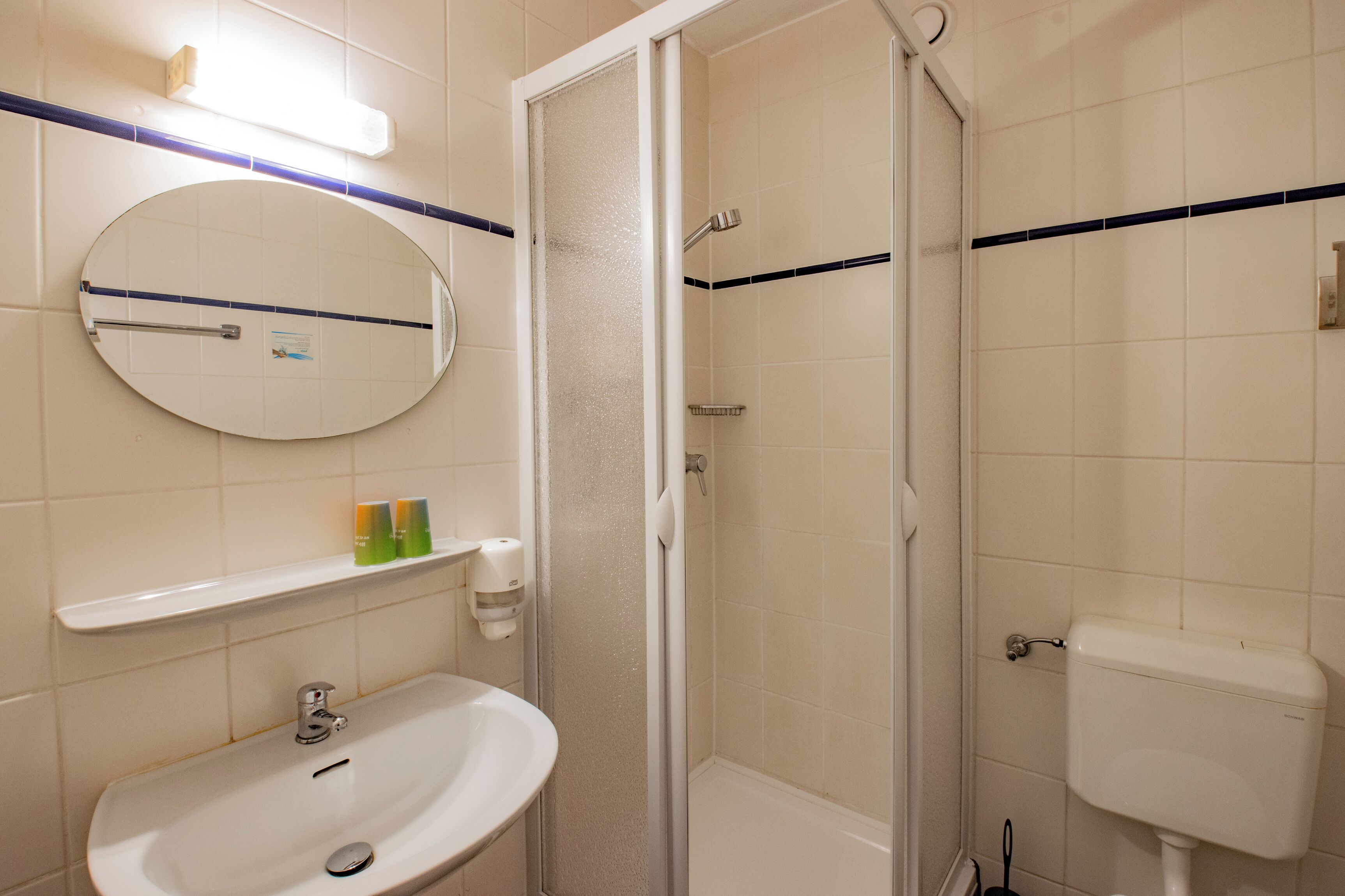 Un baño con espejo redondo, lavabo, inodoro y cabina de ducha.