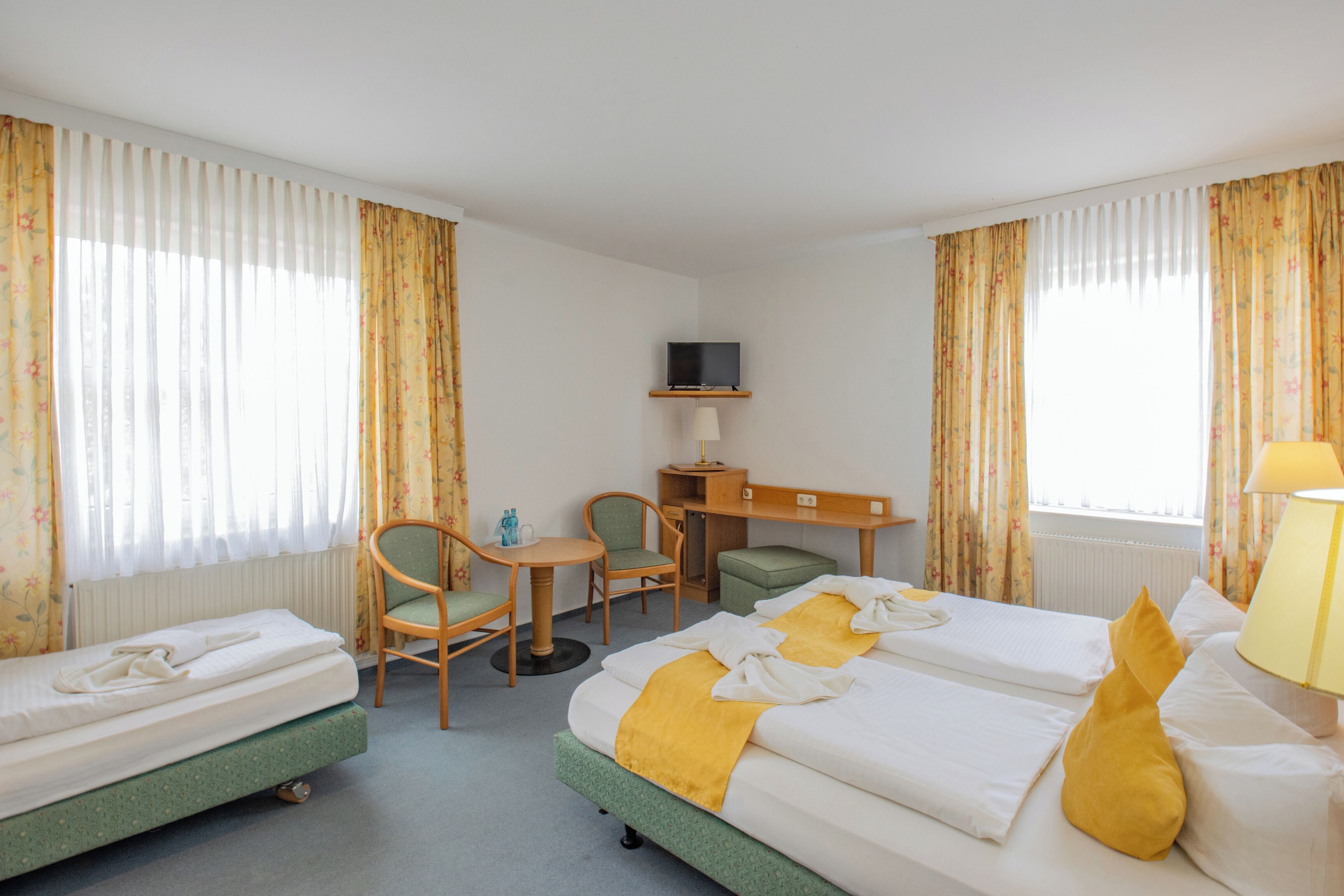 A hotel room with two beds, a desk, a chair, a television, and a window with curtains.