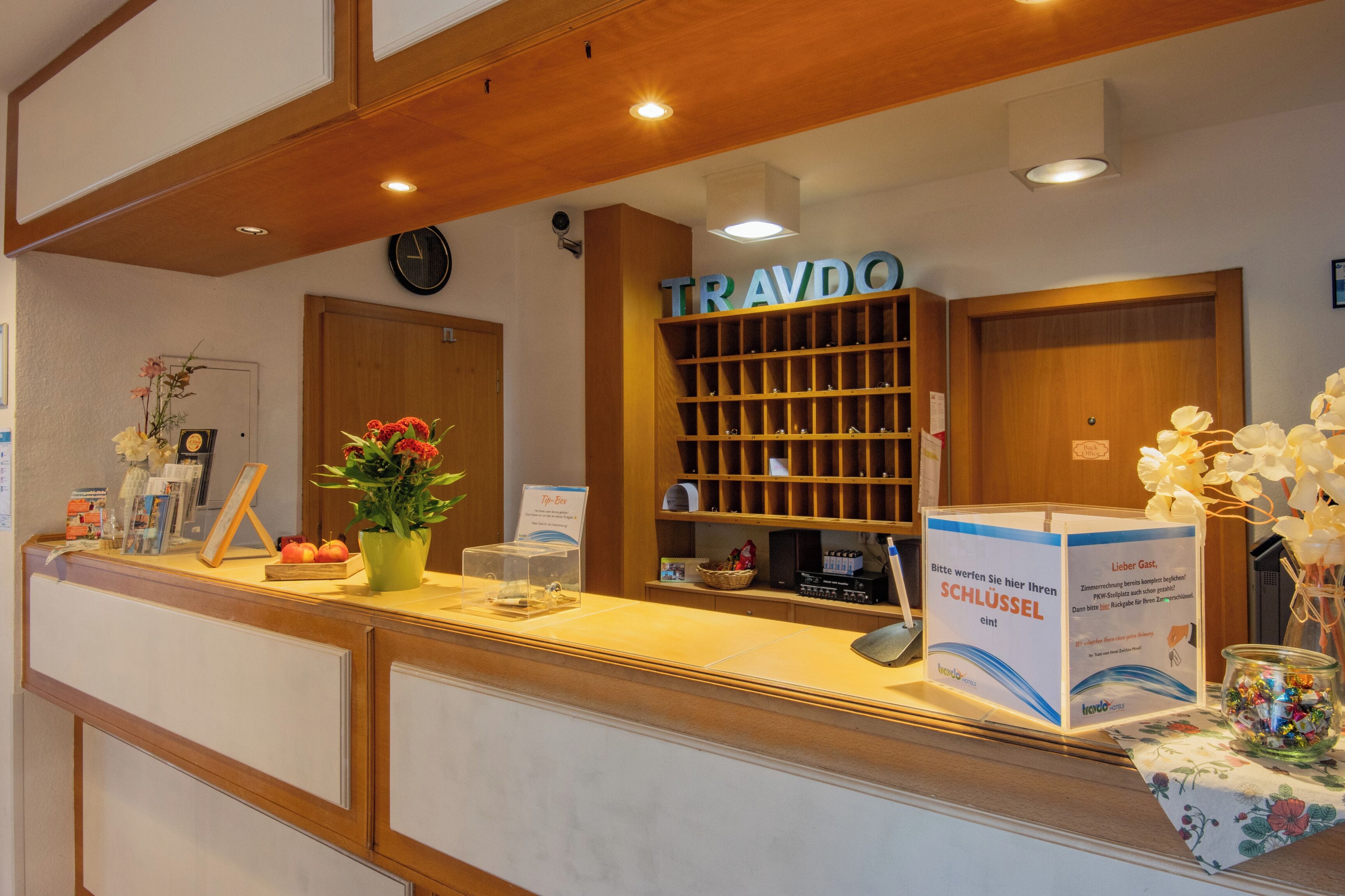 Una recepción con un letrero que dice 'TRAVDO', un reloj y un 'Top-Box' para los huéspedes.