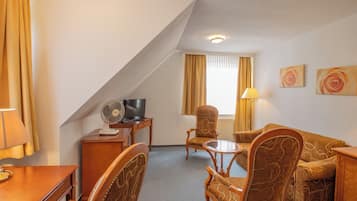 Une chambre d’hôtel comprenant un canapé, deux fauteuils, une petite table, un bureau avec une télévision et une lampe.