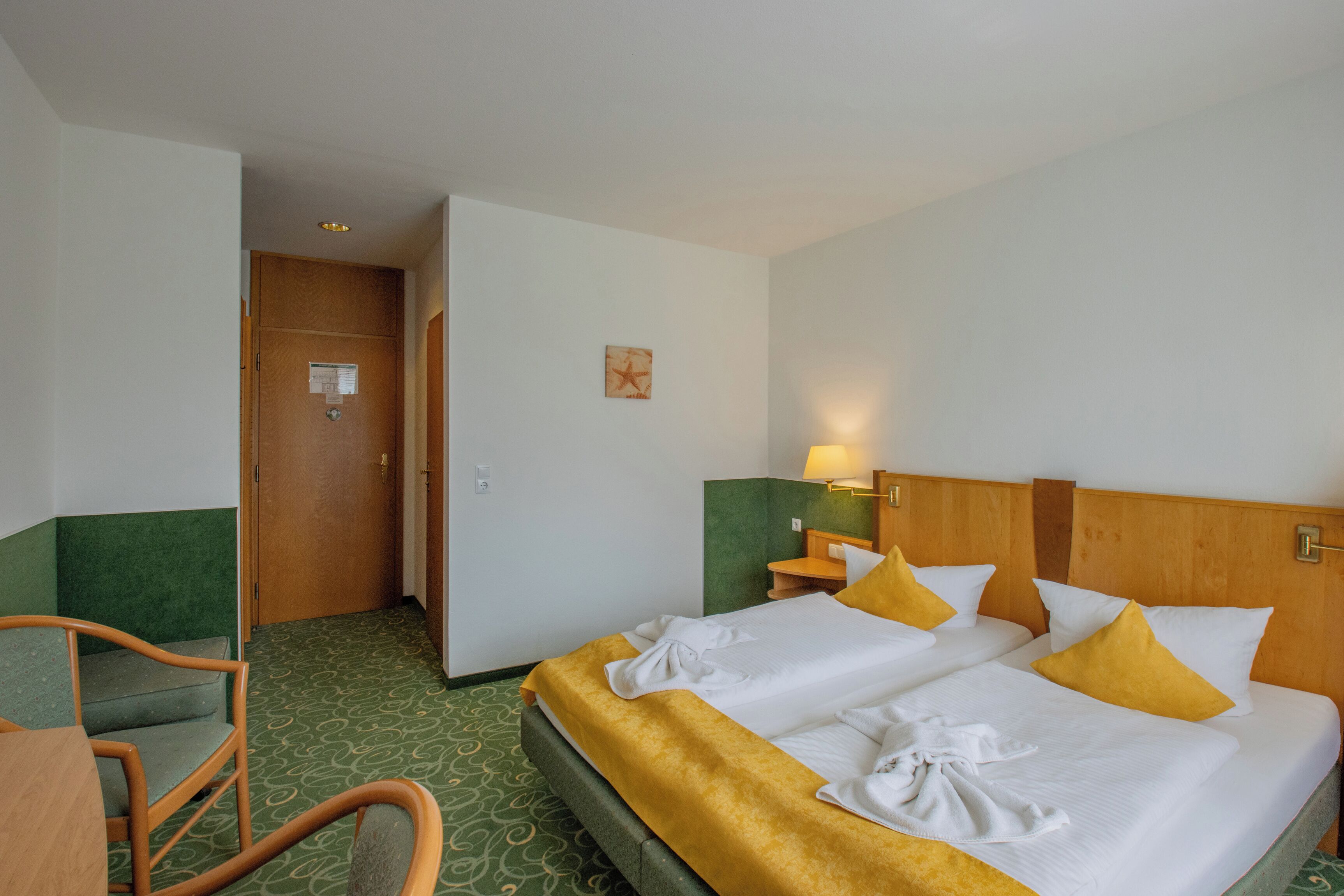 A hotel room with two beds, a desk, a chair, and a door.