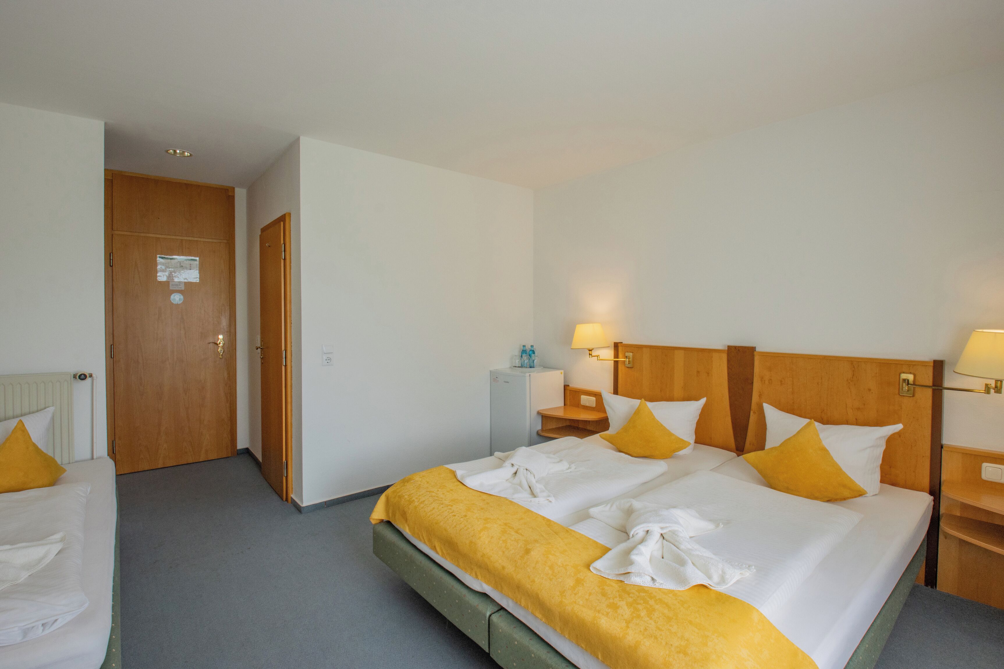 Ein Hotelzimmer mit Doppelbett, zwei Nachttischen, einem Heizkörper und einer Tür mit einem Hinweis.