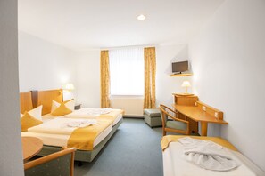 Une chambre d’hôtel avec deux lits, un bureau, une chaise, une télévision et une fenêtre avec des rideaux.