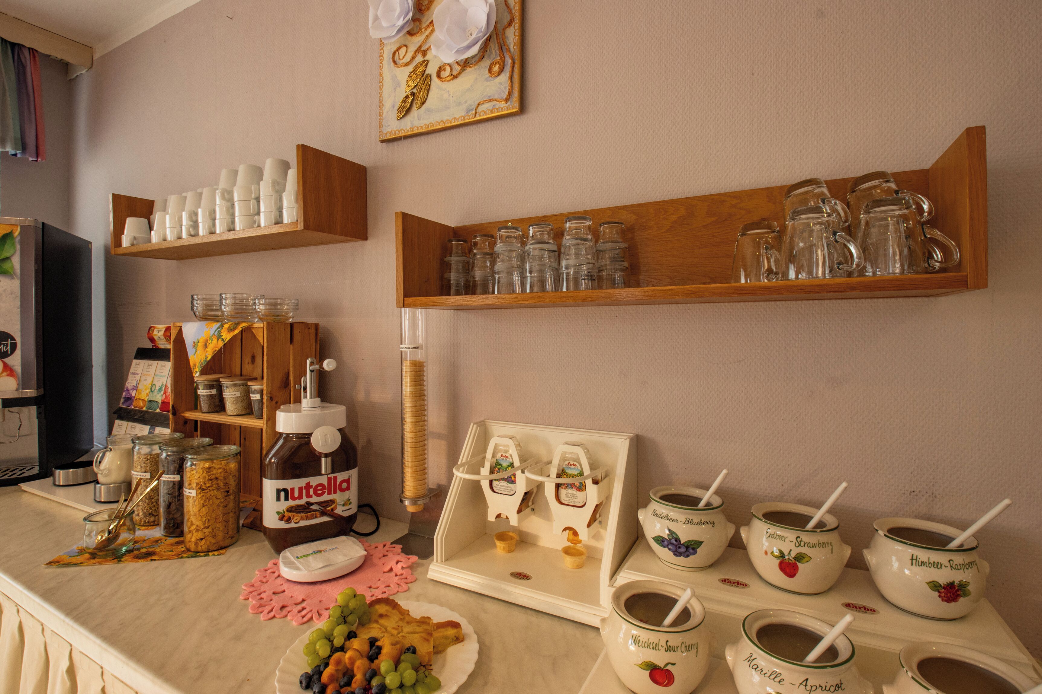Un comptoir de cuisine avec divers aliments, un distributeur de Nutella et un assortiment de verres et de tasses.