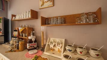 A kitchen counter with various food items, a Nutella dispenser, and a selection of glassware and mugs.