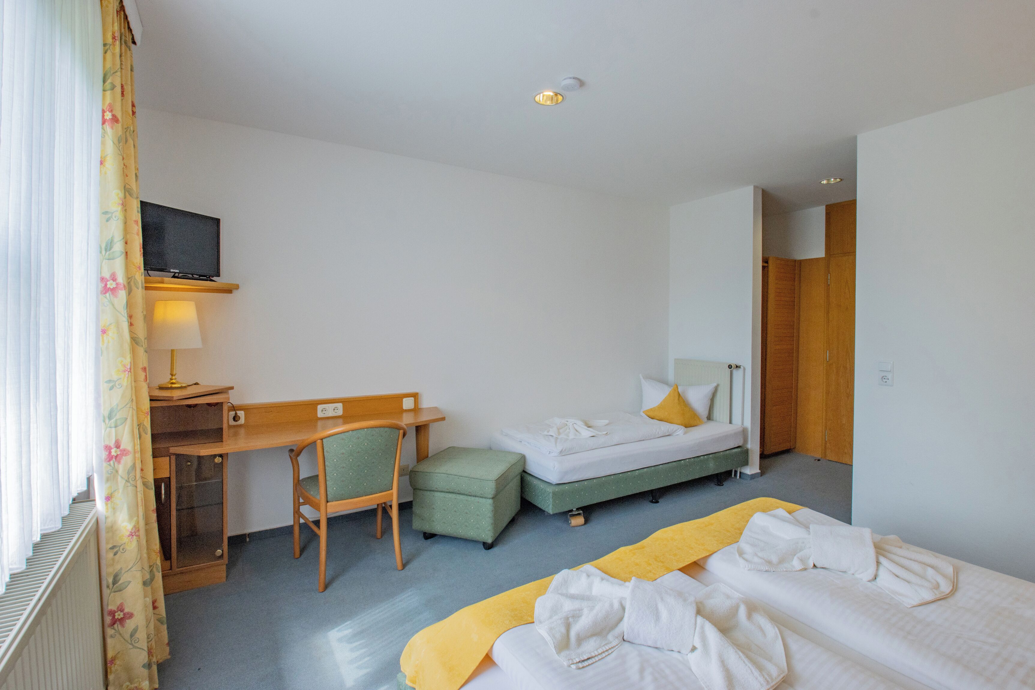 Una habitación de hotel con escritorio, dos camas, una silla, televisor y armario.