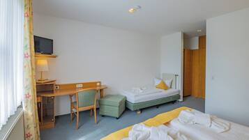 Una habitación de hotel con escritorio, dos camas, una silla, televisor y armario.