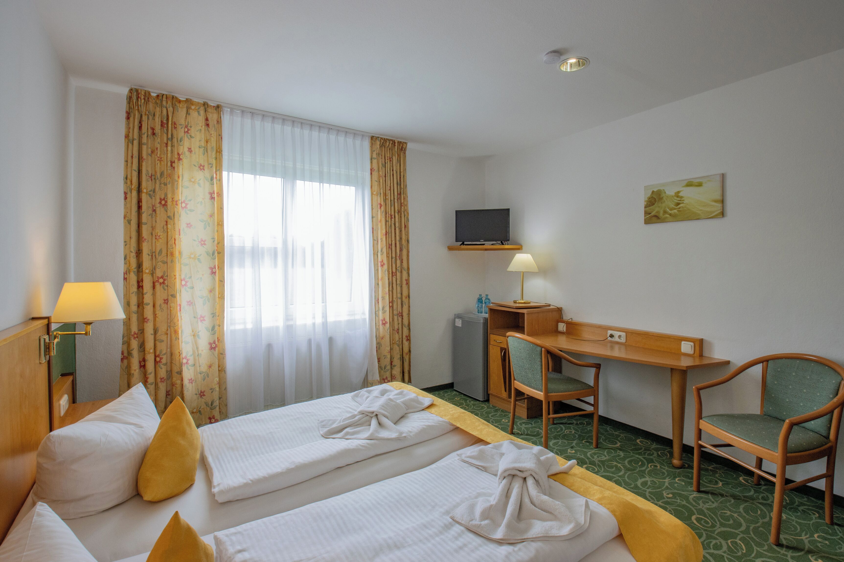 A hotel room with two beds, a desk, a chair, a television, and a small refrigerator.