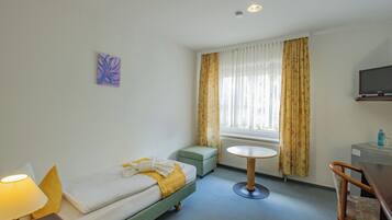 Habitación de hotel con cama, una mesita, una silla, televisor y ventana con cortinas.