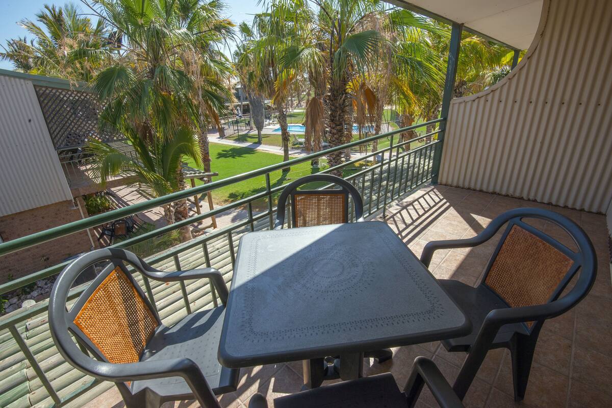 Un balcón con mesa y sillas, con vistas a una piscina y palmeras.