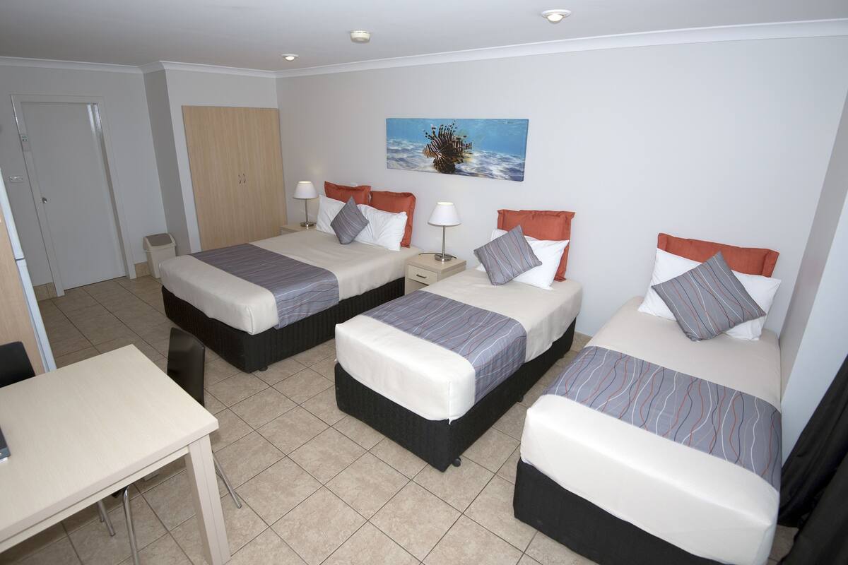 Habitación de hotel con tres camas, un escritorio y una puerta.