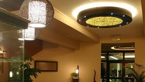 Un vestíbulo de hotel con mostrador de recepción, zona de estar y una lámpara decorativa en el techo.