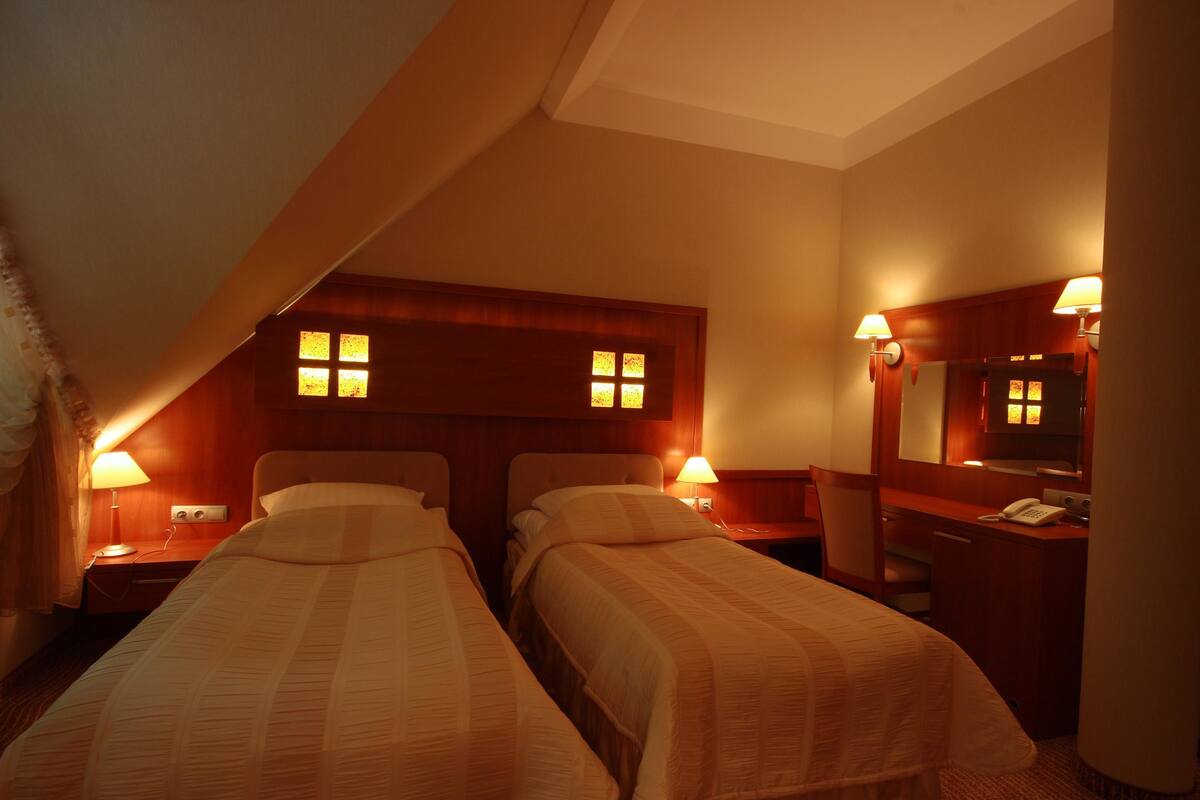 A hotel room with two single beds, a desk with a telephone, and a mirror.