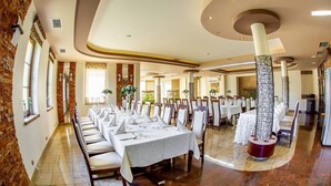 Un comedor amplio con largas mesas dispuestas para una comida, rodeado de paredes de ladrillo y grandes columnas decorativas.