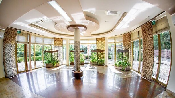 Un vestíbulo amplio con una columna central, ventanas grandes y plantas en macetas.