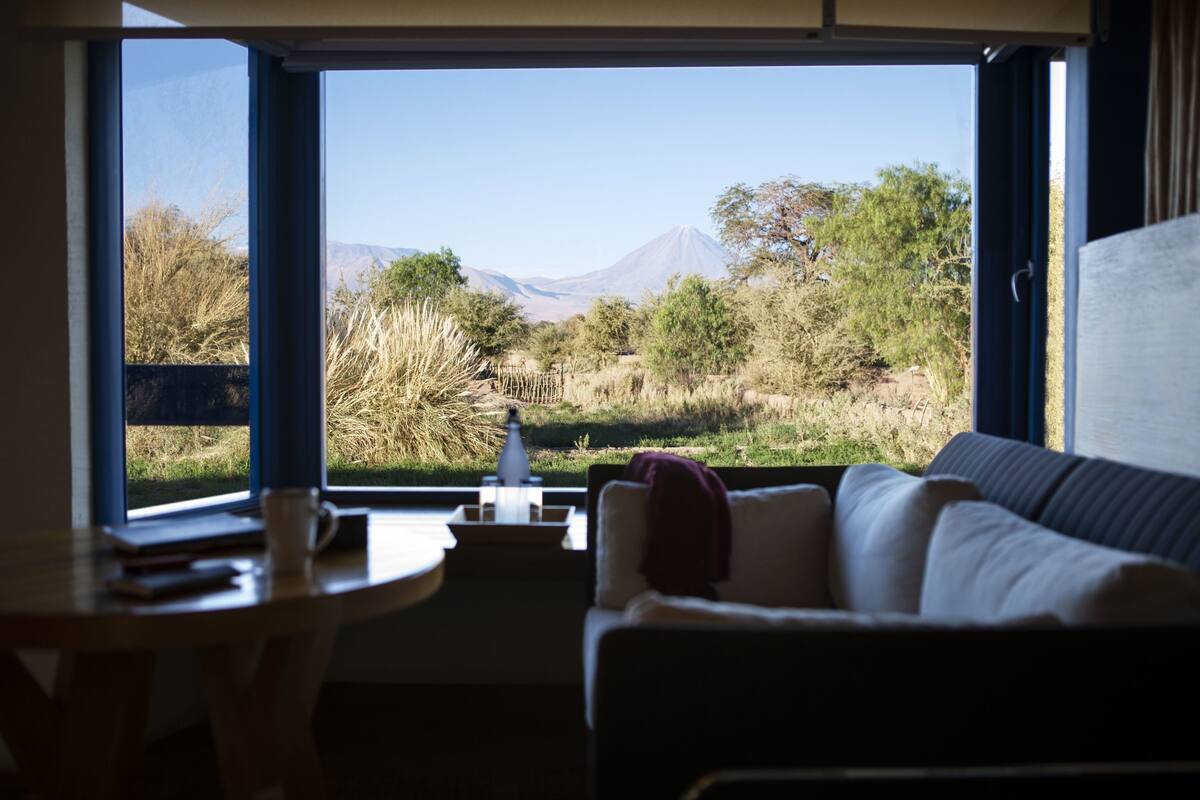 A room with a large window offering a view of a mountain and surrounding vegetation.