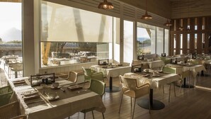 Un amplio comedor con varias mesas y sillas, ventanas grandes que ofrecen vistas al exterior e iluminación colgante.