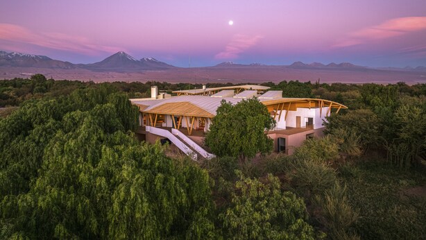 Una casa moderna con una terraza grande, rodeada de abundante vegetación y montañas al fondo.