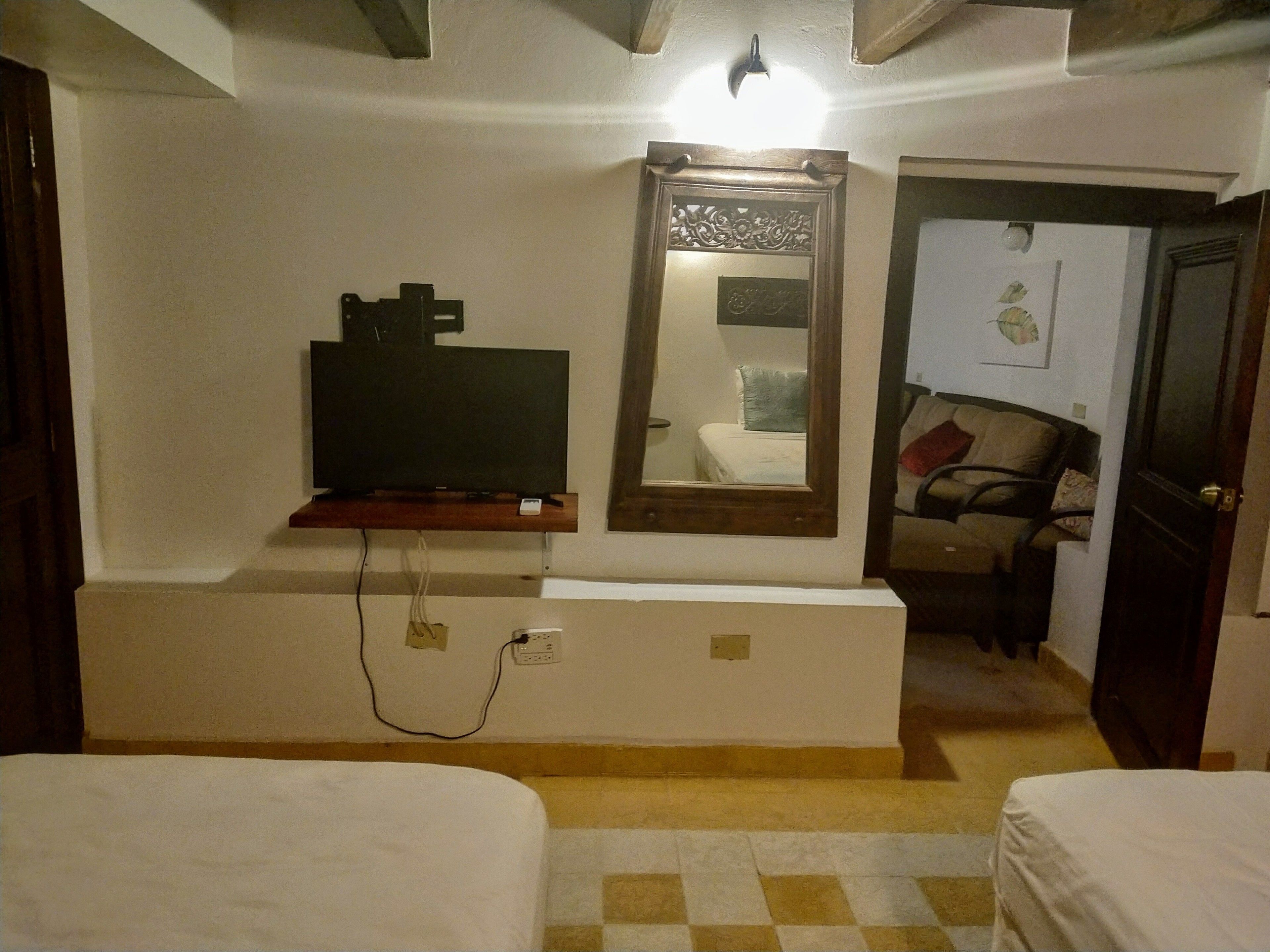 A hotel room with a TV mounted on the wall, a mirror above the bed, and a checkered floor.