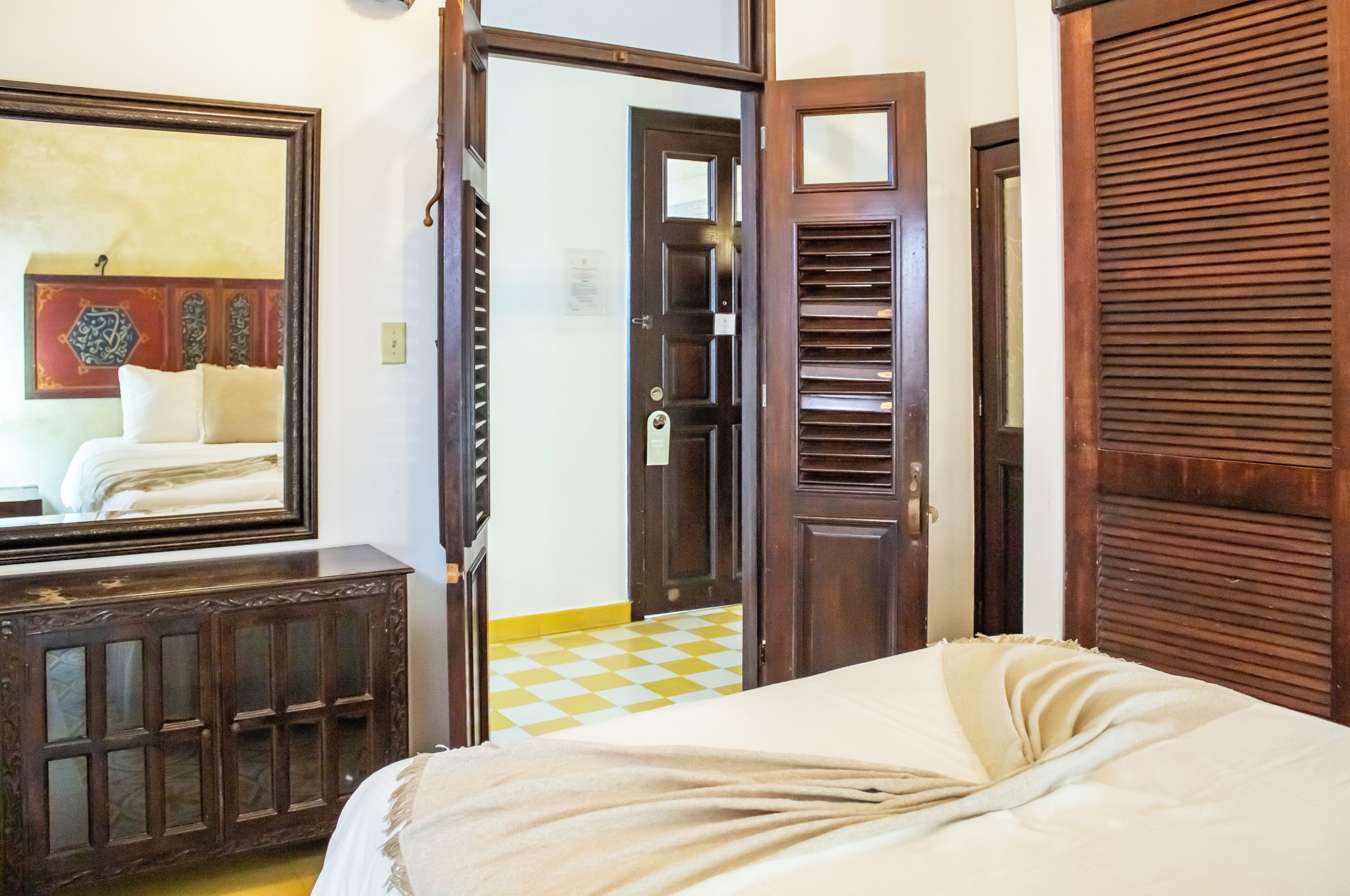 Una habitación de hotel con una cama, un armario de madera, una puerta y un suelo a cuadros.