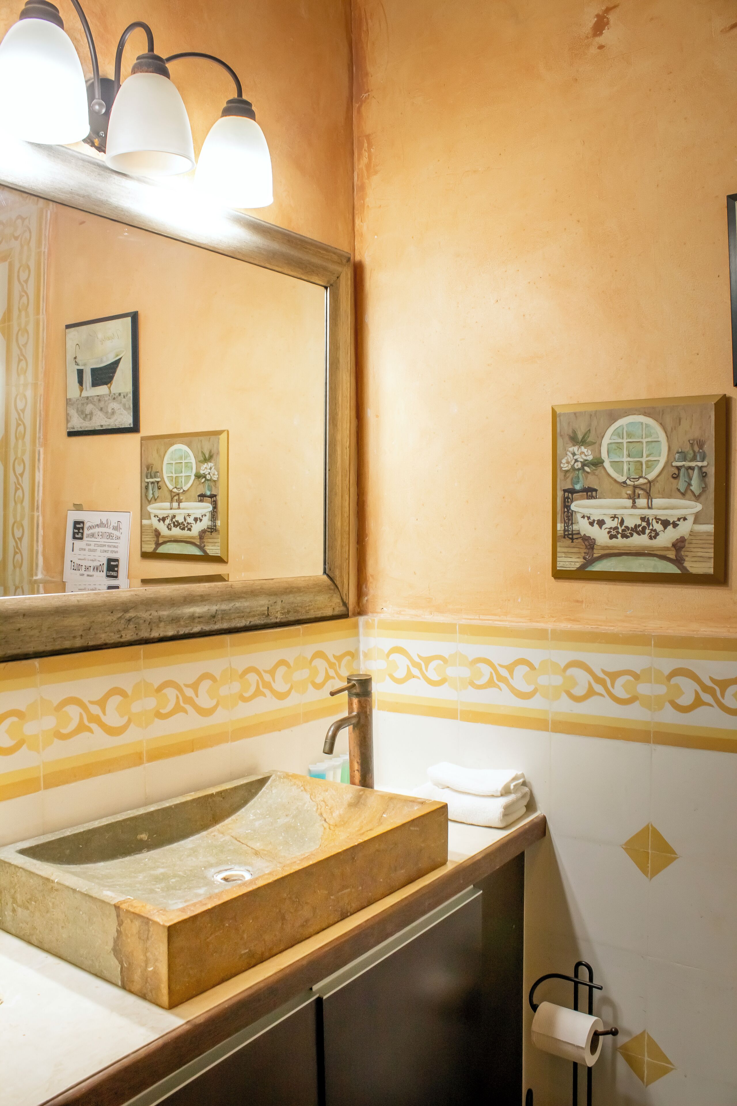 Een badkamer met een houten wastafelmeubel, een grote spiegel en een toiletrolhouder aan de muur.