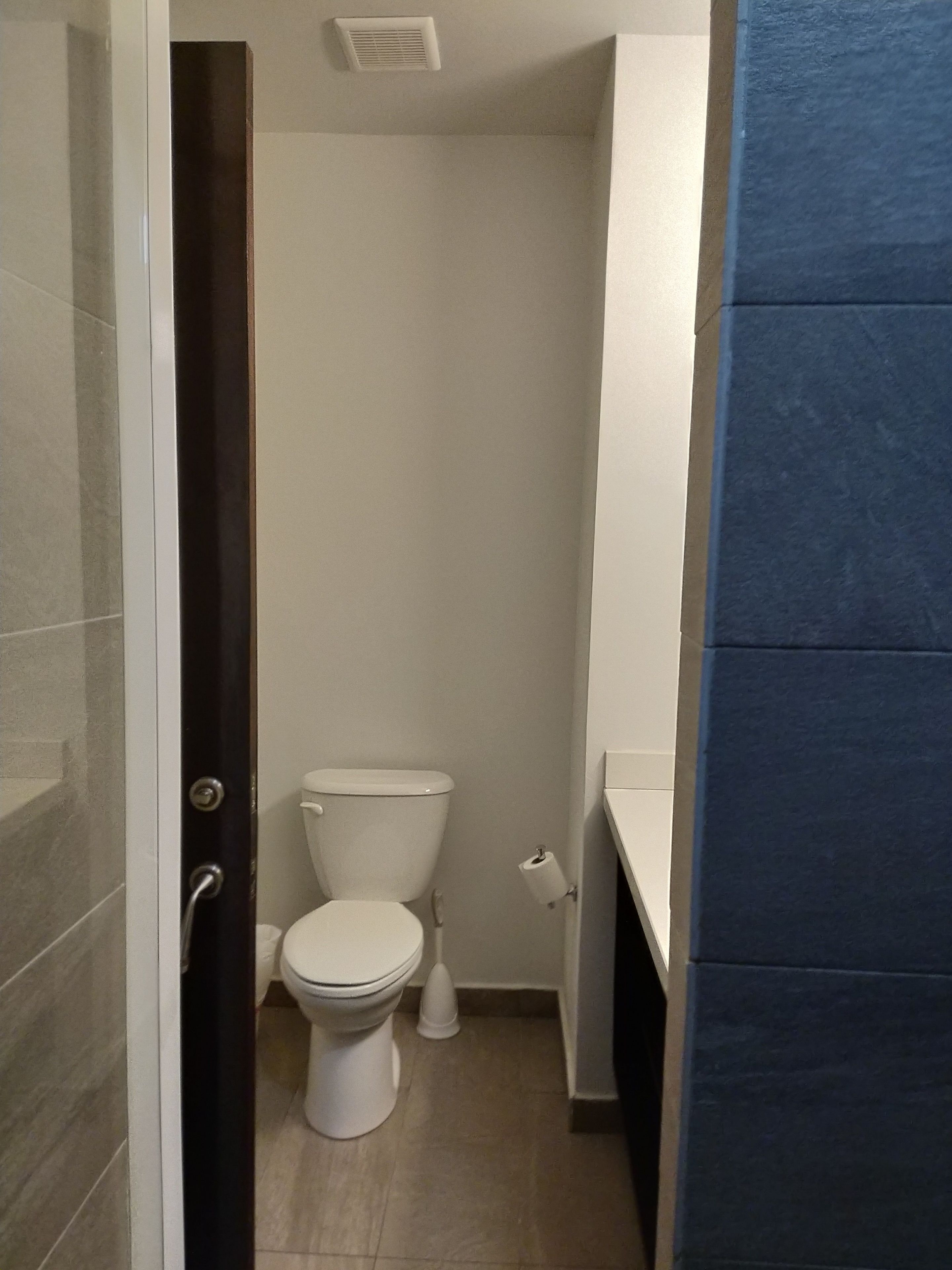 Ein kleines, schmales Badezimmer mit Toilette, Waschbecken und Duschbereich.