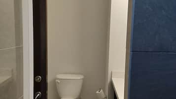 Un baño pequeño y estrecho con inodoro, lavamanos y zona de ducha.